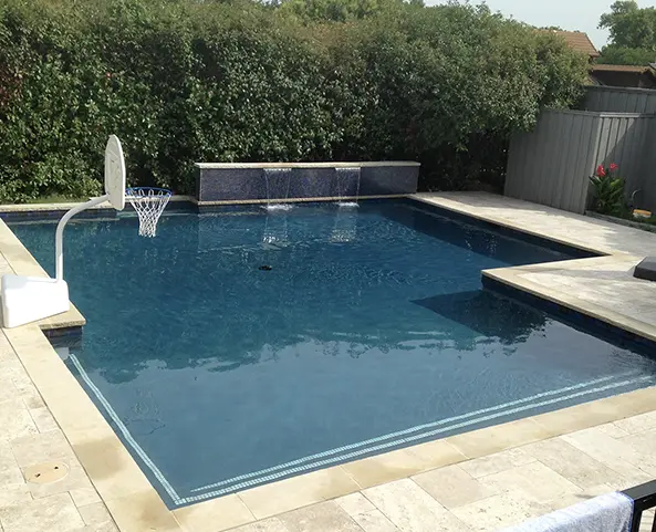 Modern rectangular swimming pool with stone decking and water feature in a residential backyard