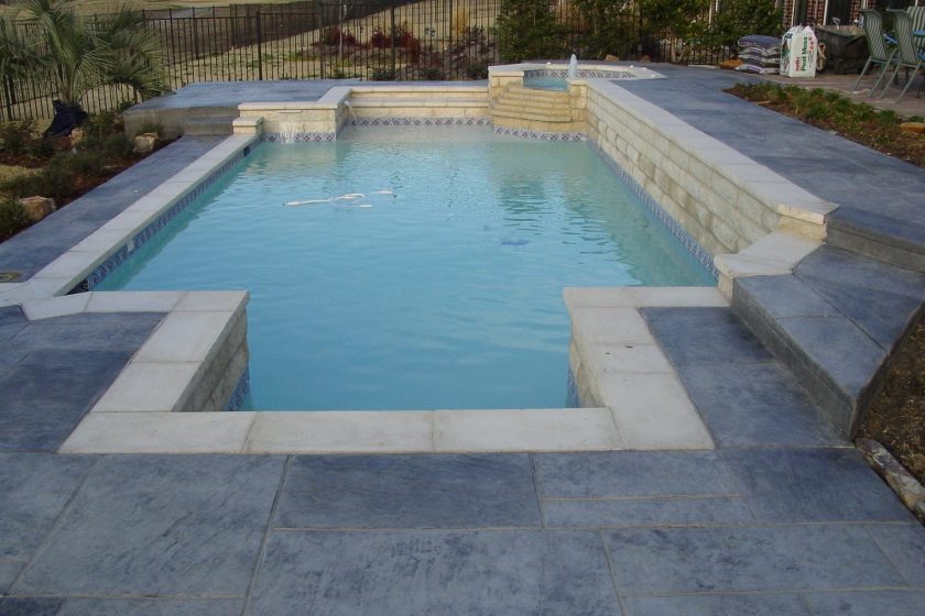 Straight-line pool with an Austin stone raised beam, Cordova cream coping and stamped concrete decking, built by Hobert Pools & Spas