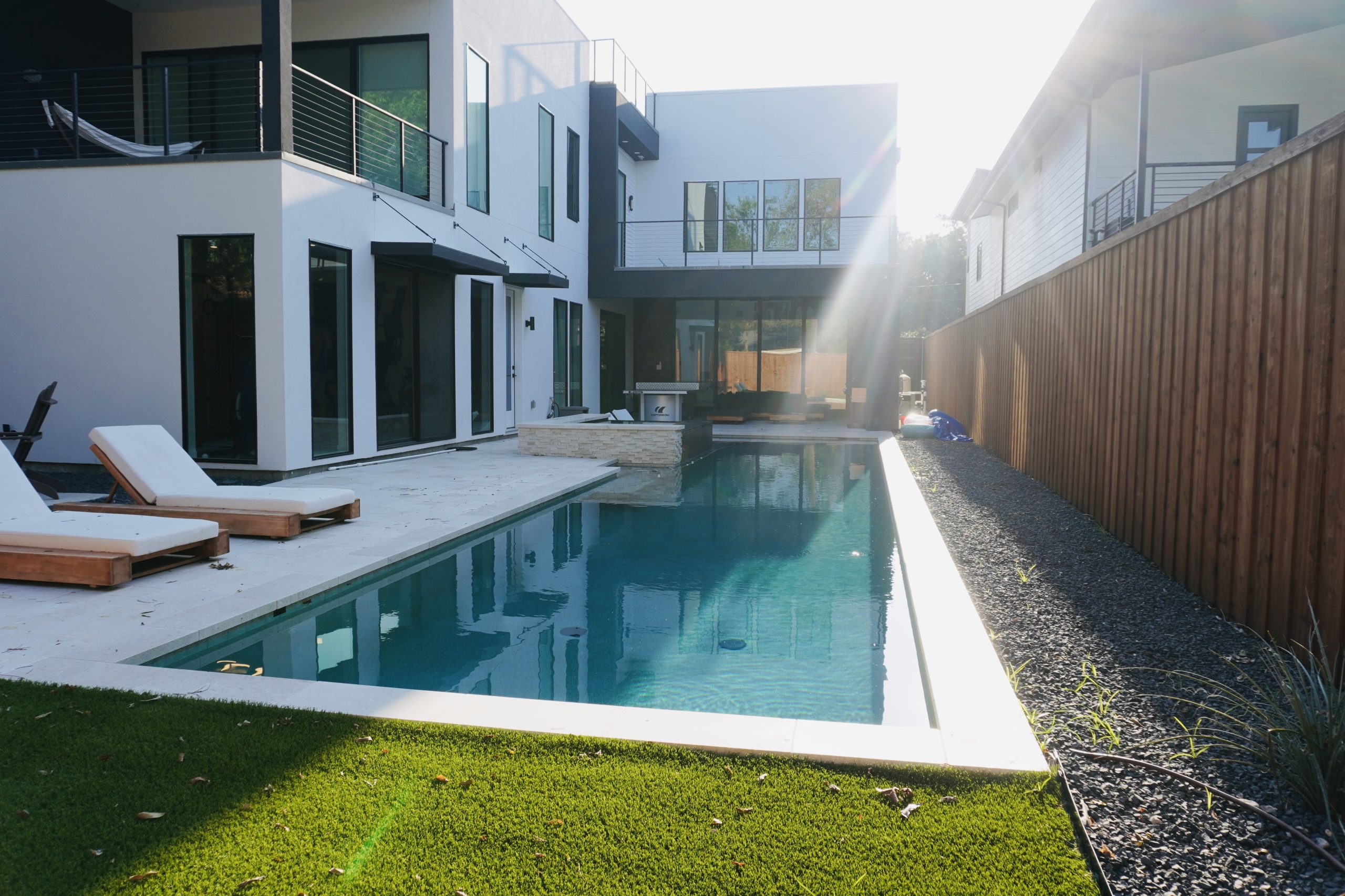 Long rectangular pool beside a modern home with lounge chairs and turf, built by Hobert Pools & Spas