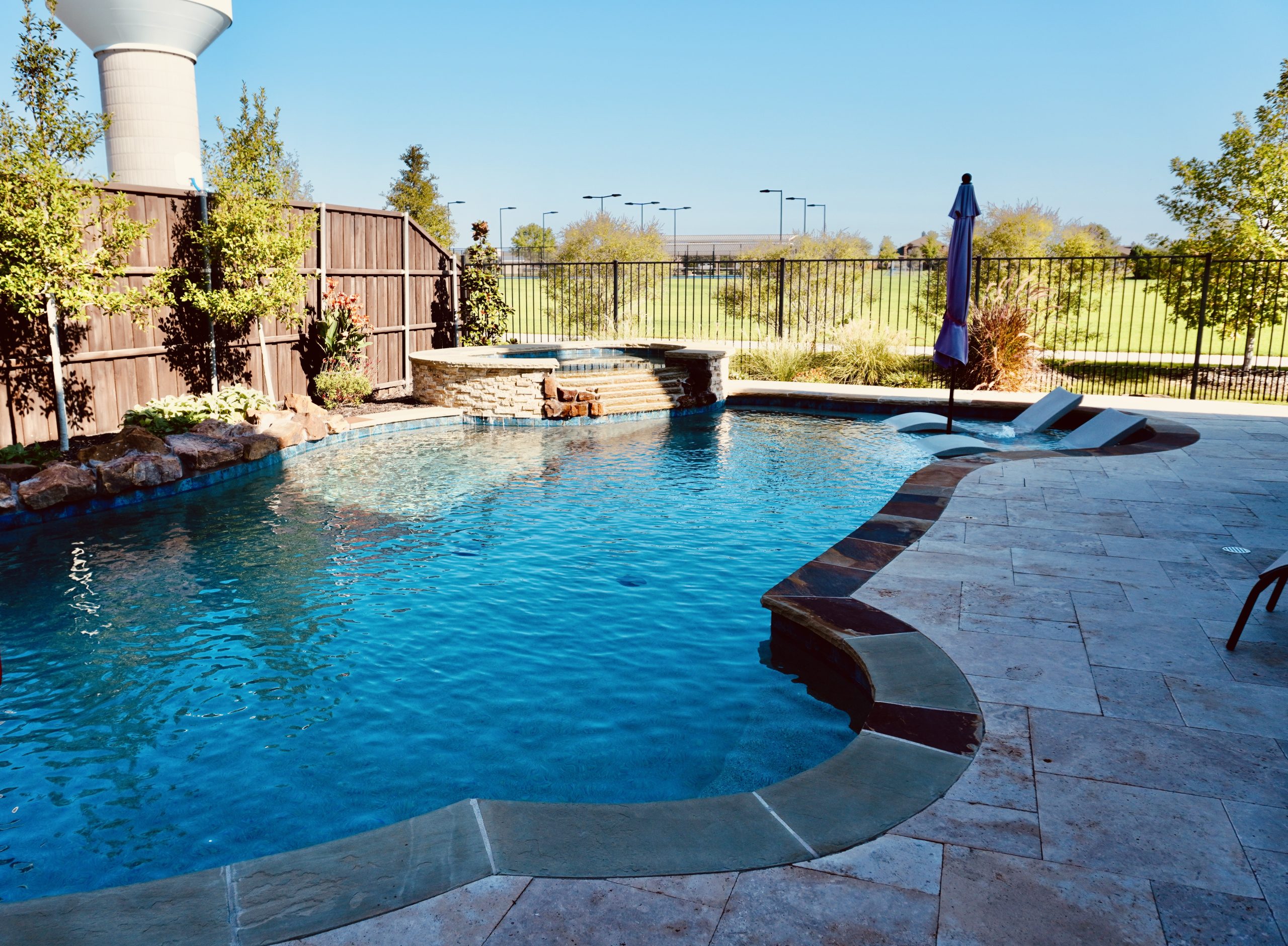 Freeform pool with a raised stone spa, tanning ledge loungers and travertine coping, built by Hobert Pools & Spas