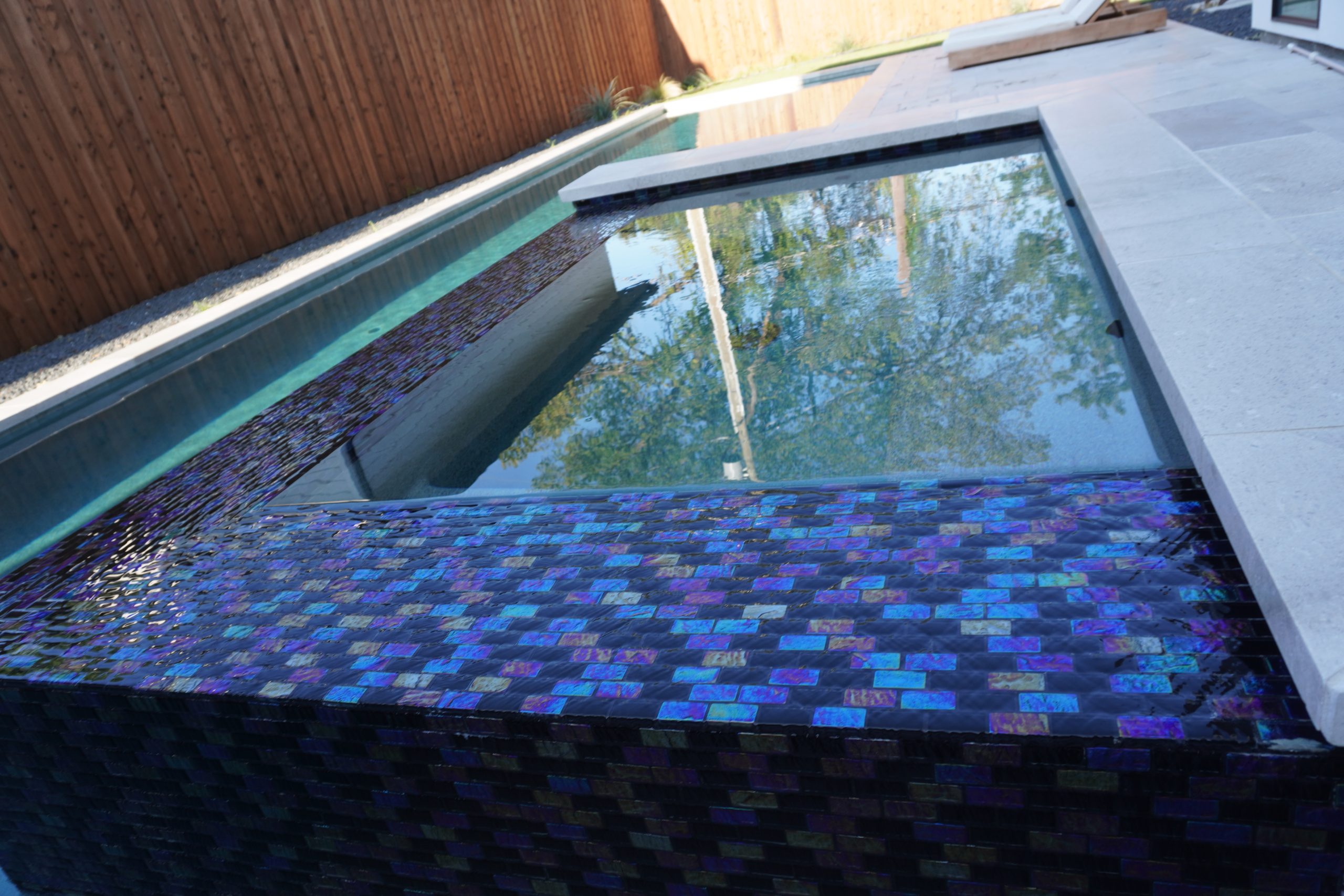 Raised spa finished in blue glass tile with light stone coping, built by Hobert Pools & Spas