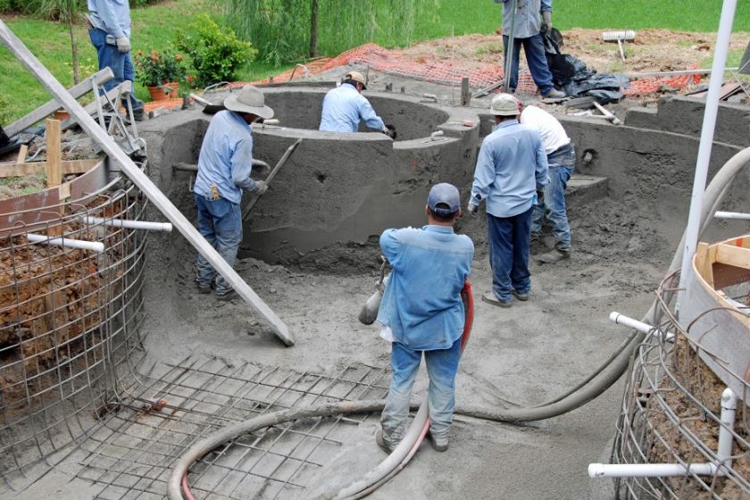 Hobert Pools crew applying gunite to a pool and spa shell over steel reinforcement