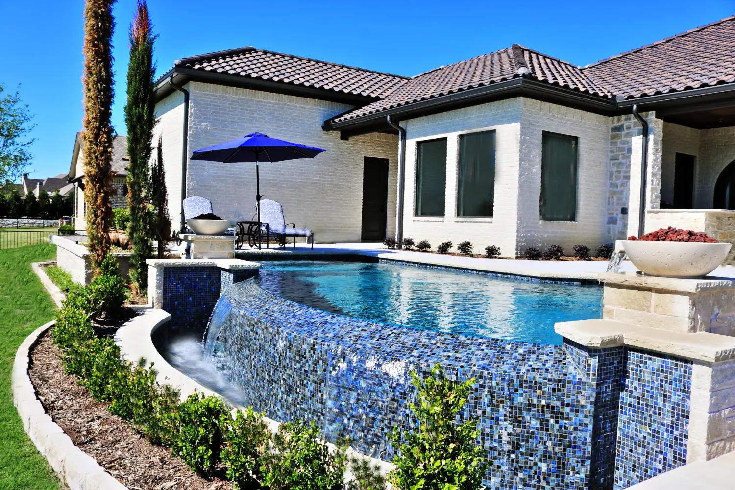 Vanishing edge gunite pool with a glass tile spillover wall and fire bowls, built by Hobert Pools and Spas
