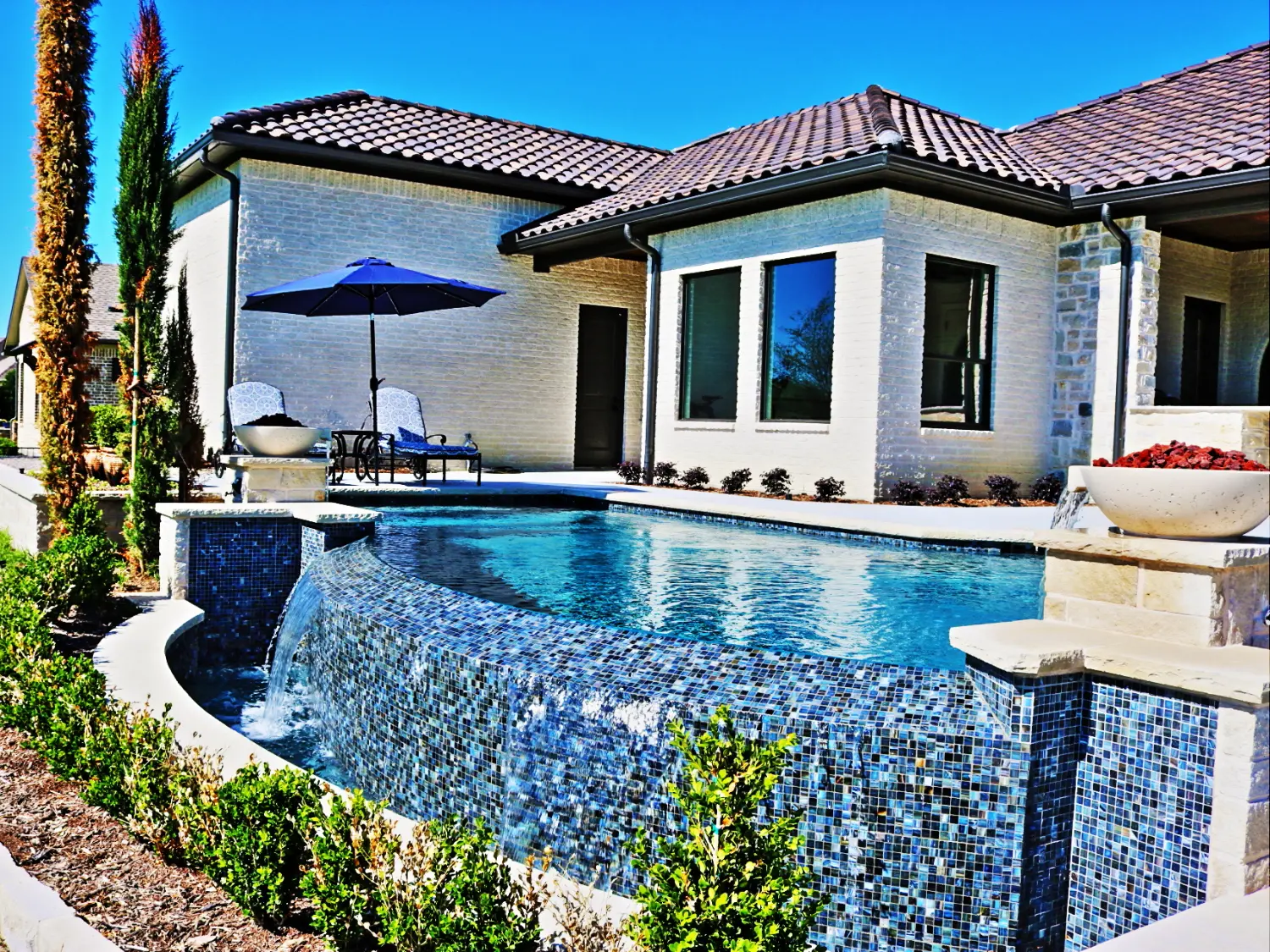 Vanishing edge pool with a blue glass tile spillover wall and a fire bowl, built by Hobert Pools & Spas