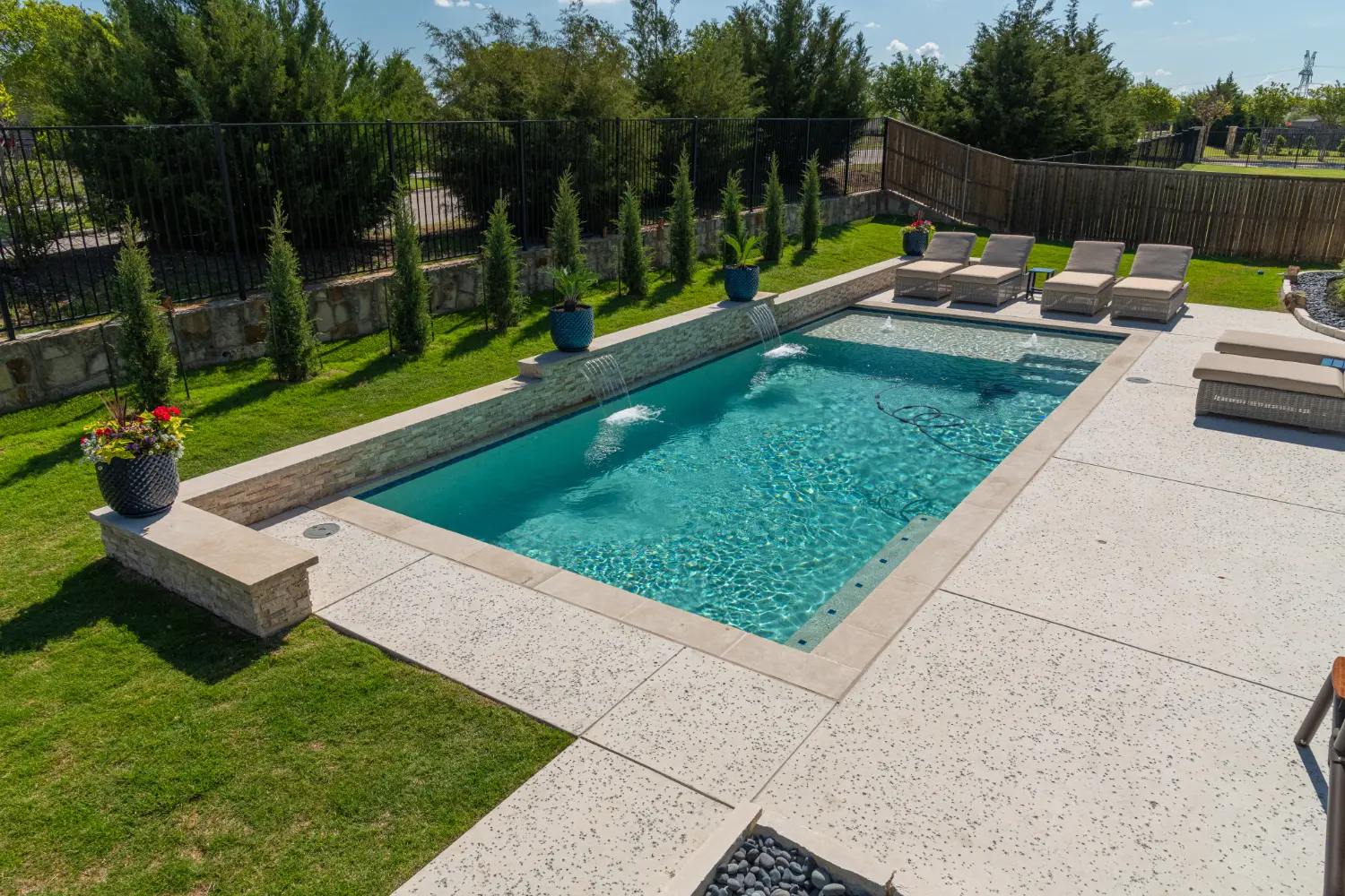 Rectangular gunite pool with a stone raised wall, sheer descents and an aggregate deck, built by Hobert Pools and Spas