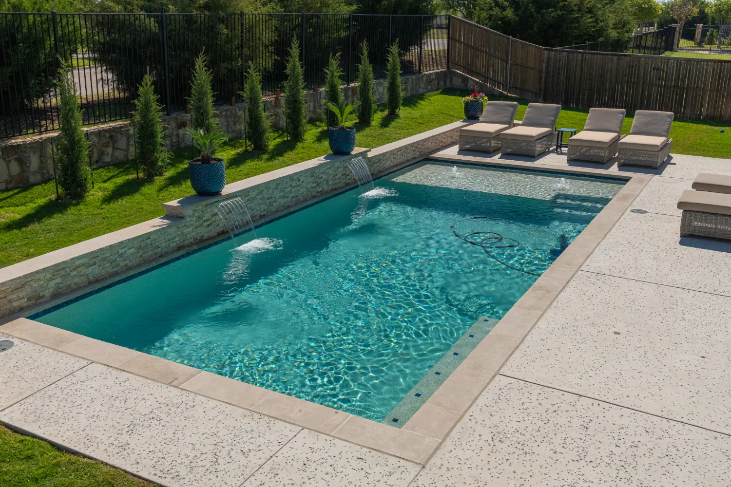 Rectangular pool with a stone raised wall, sheer descent waterfalls and an exposed aggregate deck, built by Hobert Pools & Spas