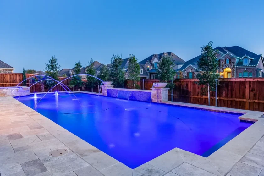 Rectangular pool with arcing laminar jets and a travertine deck at dusk, built by Hobert Pools & Spas