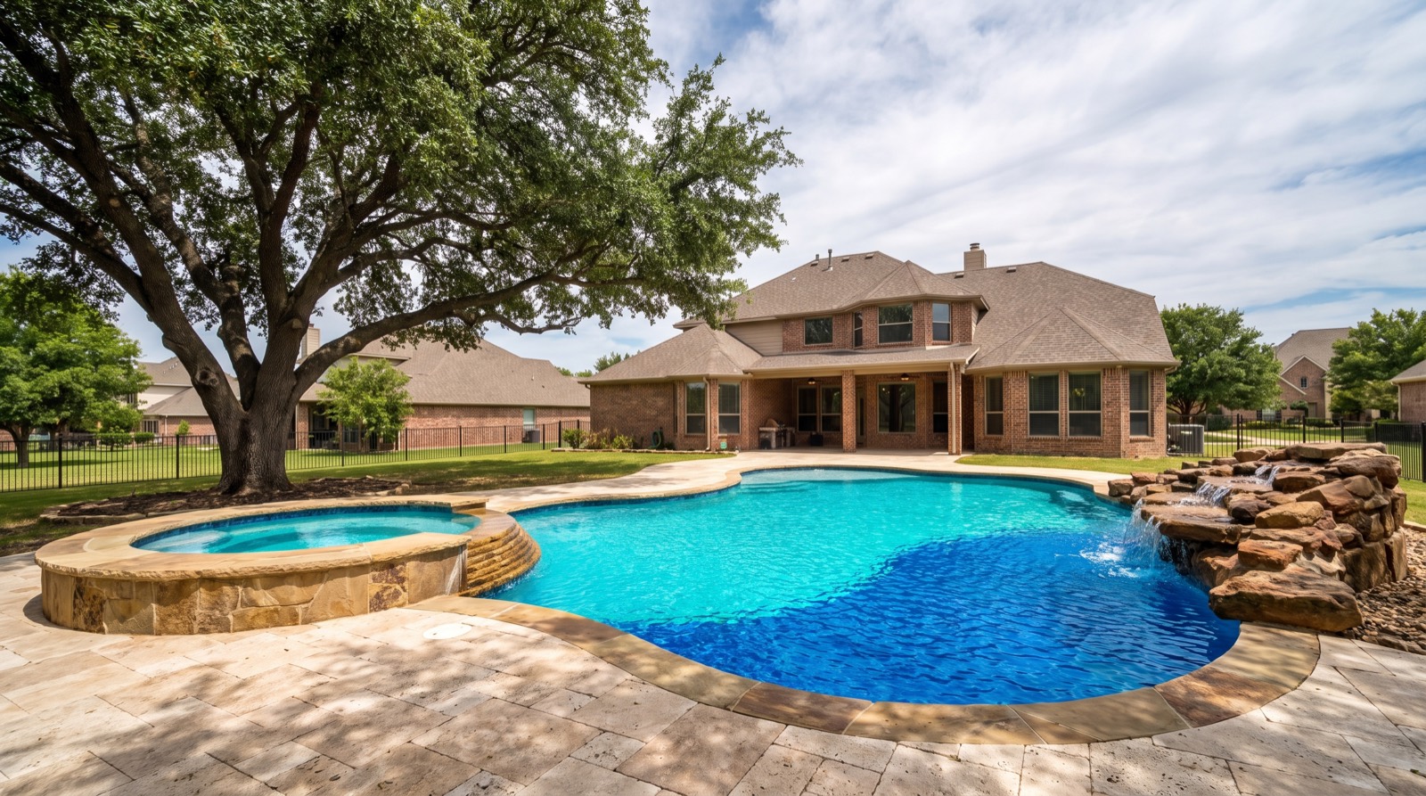 Freeform gunite pool with a raised spa and travertine patio in a Dallas backyard